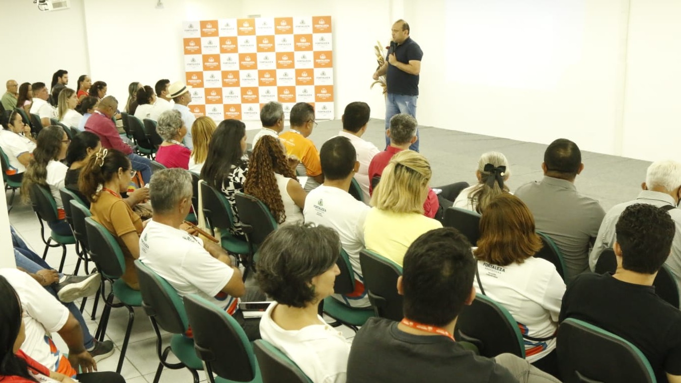 A foto mostra pessoas em um auditório assistindo a formação